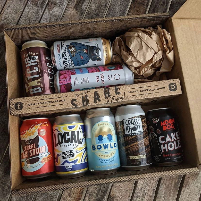 A variety of craft beer cans are displayed inside a cardboard box with the text 'SHARE' visible on the inner flap. The cans are adorned with different logos and colors, indicating a selection of unique beers.